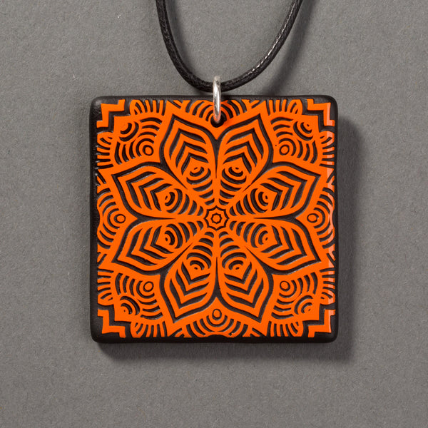 Sandcarved bright orange and black glass flower mandala pendant.