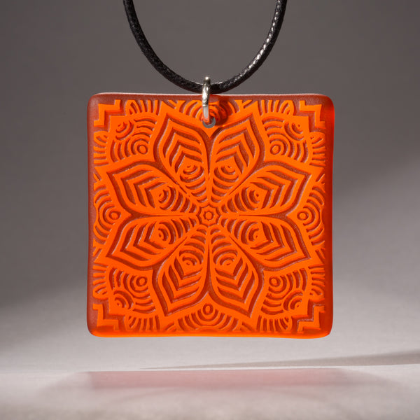 Sandcarved bright orange and orange transparent glass flower mandala pendant.