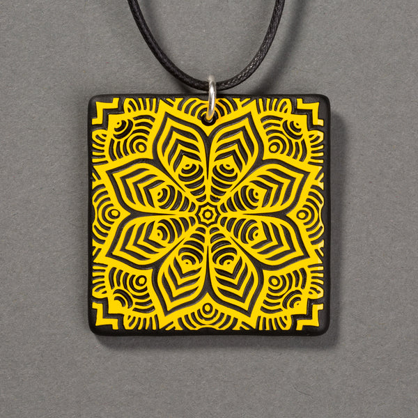 Sandcarved yellow and black glass flower mandala pendant.