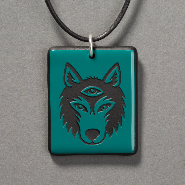 Sandcarved aquamarine and black glass silicate wolf logo pendant.