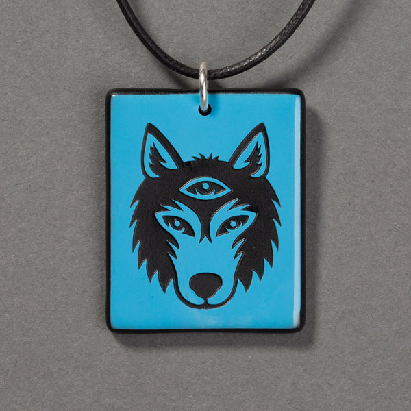 Sandcarved deep sky blue and black glass silicate wolf logo pendant.