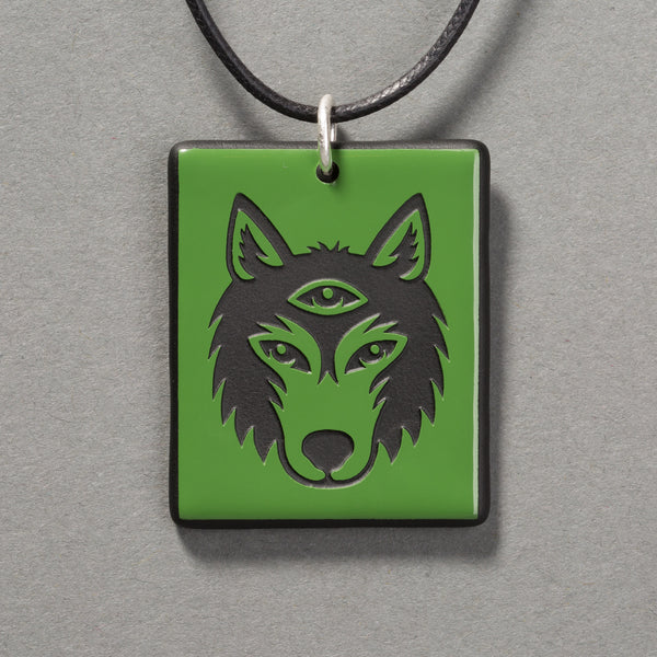 Sandcarved green and black glass silicate wolf logo pendant.