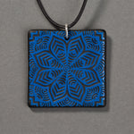 Sandcarved blue and black glass flower mandala pendant.