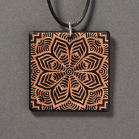 Sandcarved bronze and black glass flower mandala pendant.