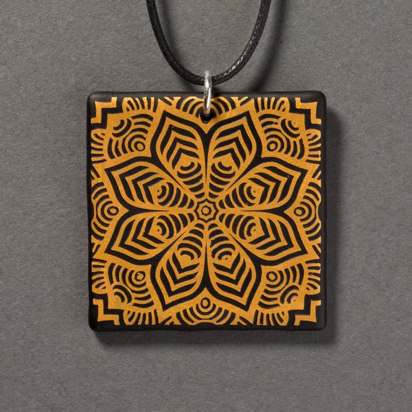 Sandcarved gold and black glass flower mandala pendant.