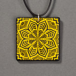 Sandcarved yellow and black glass flower mandala pendant.