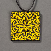 Sandcarved yellow and black glass flower mandala pendant.